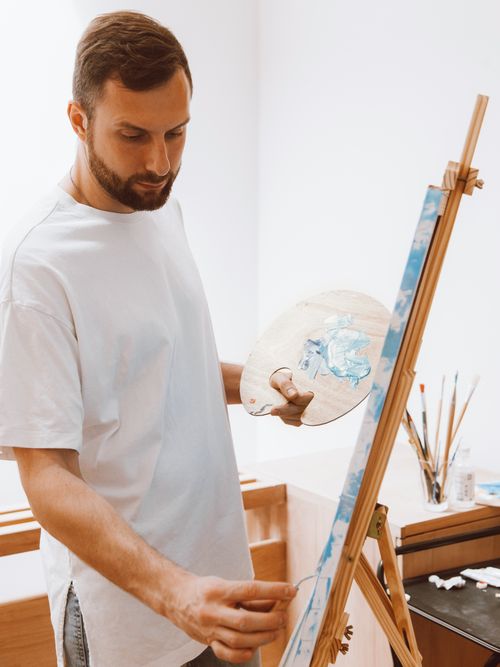Free Man in a studio painting on an easel with a palette, focused and creative. Stock Photo