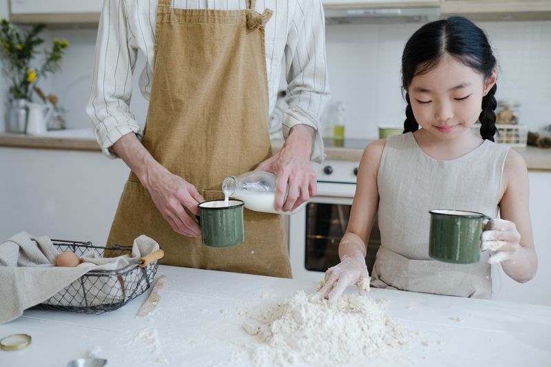 Girl helping a parent prepare dough in the kitchen