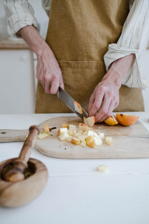 Free Person slicing apples on a wooden cutting board in a modern kitchen setting. Stock Photo