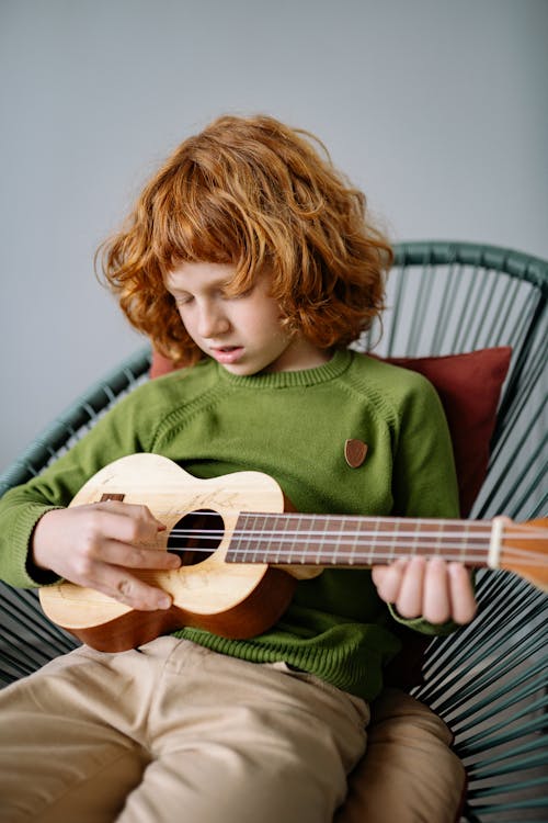 Photo gratuite de chaise en bois, enfant, être assis, garçon, guitare,  individu, instrument à cordes, instrument de musique, jambes croisées,  jeune, jouer, mur de béton