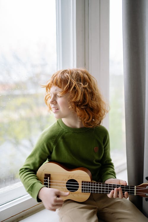 A Redheaded Boy Playing a Ukulele while Sitting