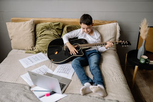 Boy Sitting on Bed While Learning to Play Guitar