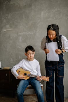 Boy learning ukulele with music teacher guidance, indoors setting.