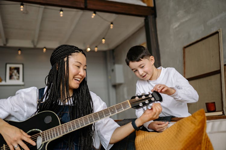 A Child Looking At A Happy Woman Playing A Guitar