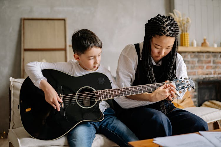 Woman Teaching A Young Boy How To Play A Guitar