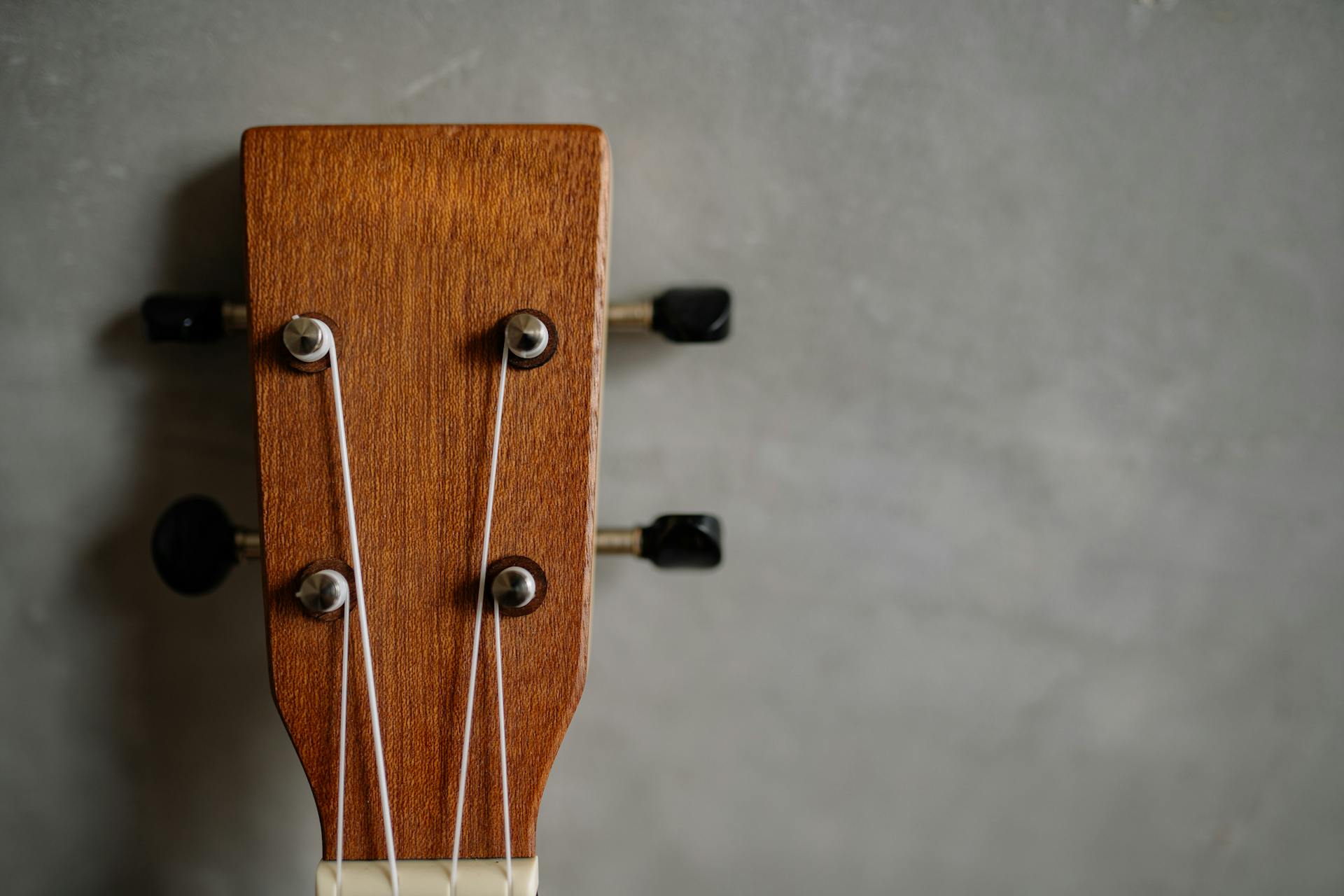 Wooden ukulele headstock close-up showing tuning pegs against a gray background.