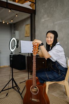 Young woman with braided hair posing with a guitar in a modern home studio.