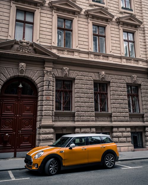 Free A vibrant yellow car parked in front of a historical building facade in an urban area. Stock Photo