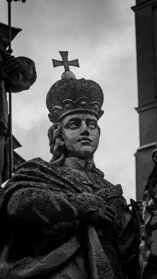 Free Black and white close-up of a crowned statue with a cross against a cloudy sky. Stock Photo