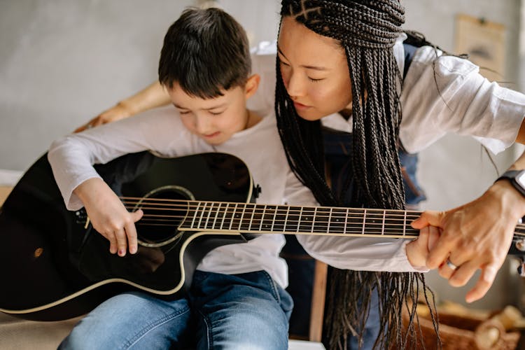 Woman Teaching A Kid To Play A Guitar