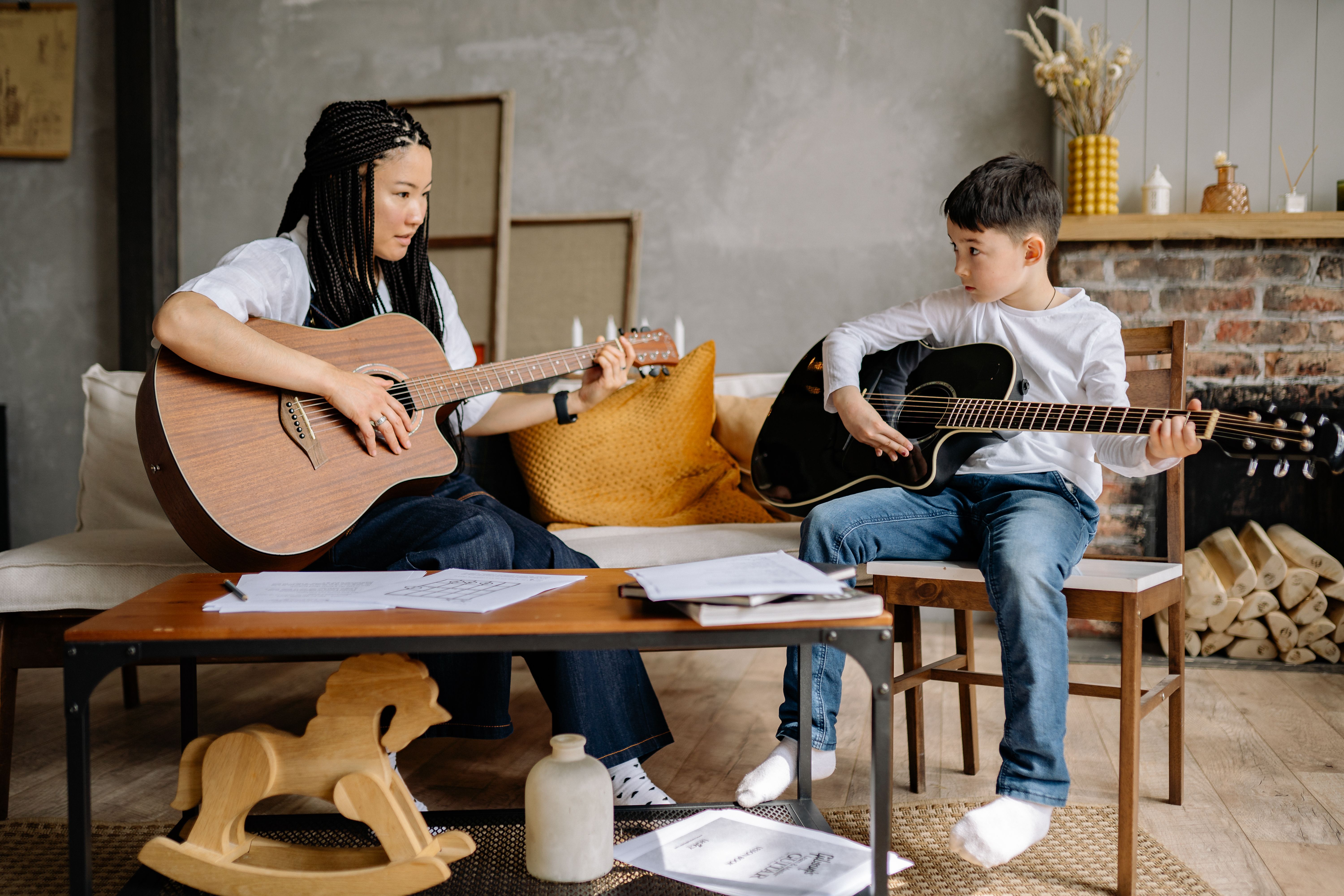 A woman teaches a boy to play guitar at home, fostering musical skills and creativity.
