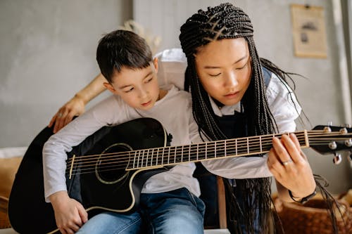 Free Woman with Braided Hair Teaching a Boy in Playing Guitar Stock Photo