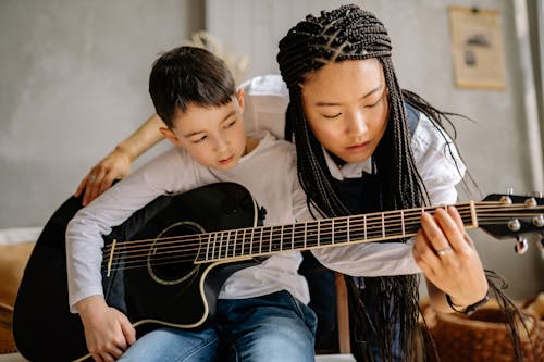 Woman with Braided Hair Teaching a Boy in Playing Guitar