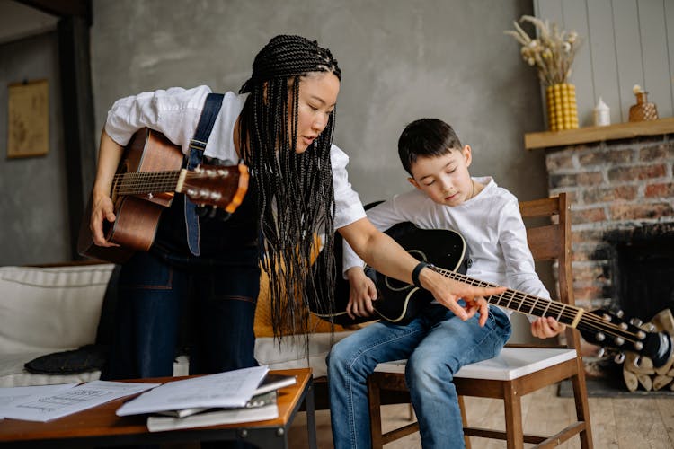 A Music Instructor With Braided Hair Teaching A Boy  To Play Guitar