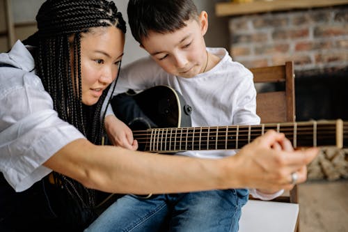 Close Up Photo of a Woman Teaching a Boy in Playing Guitar