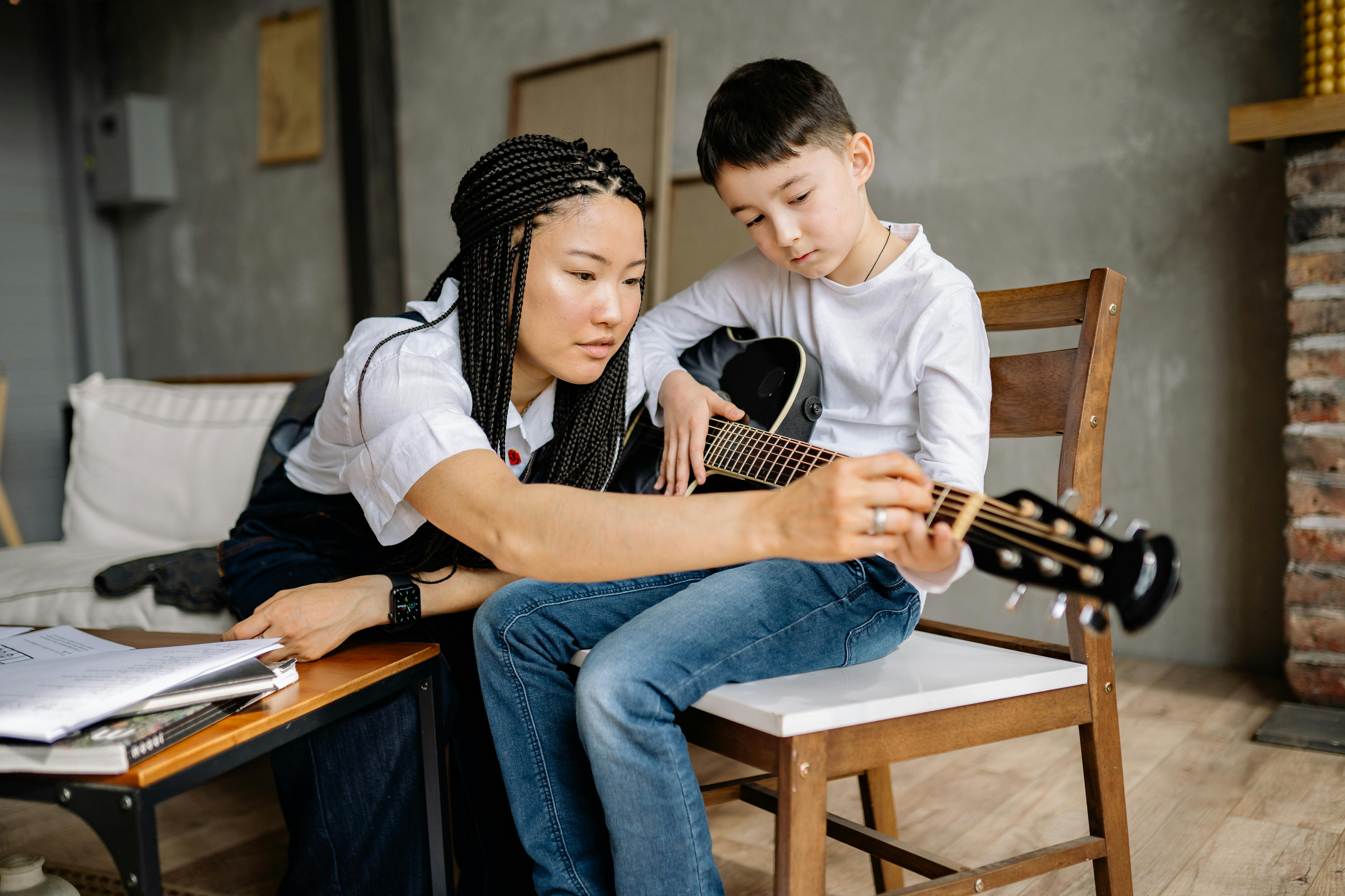 A child learning to play guitar with a teacher in a cozy home setting.