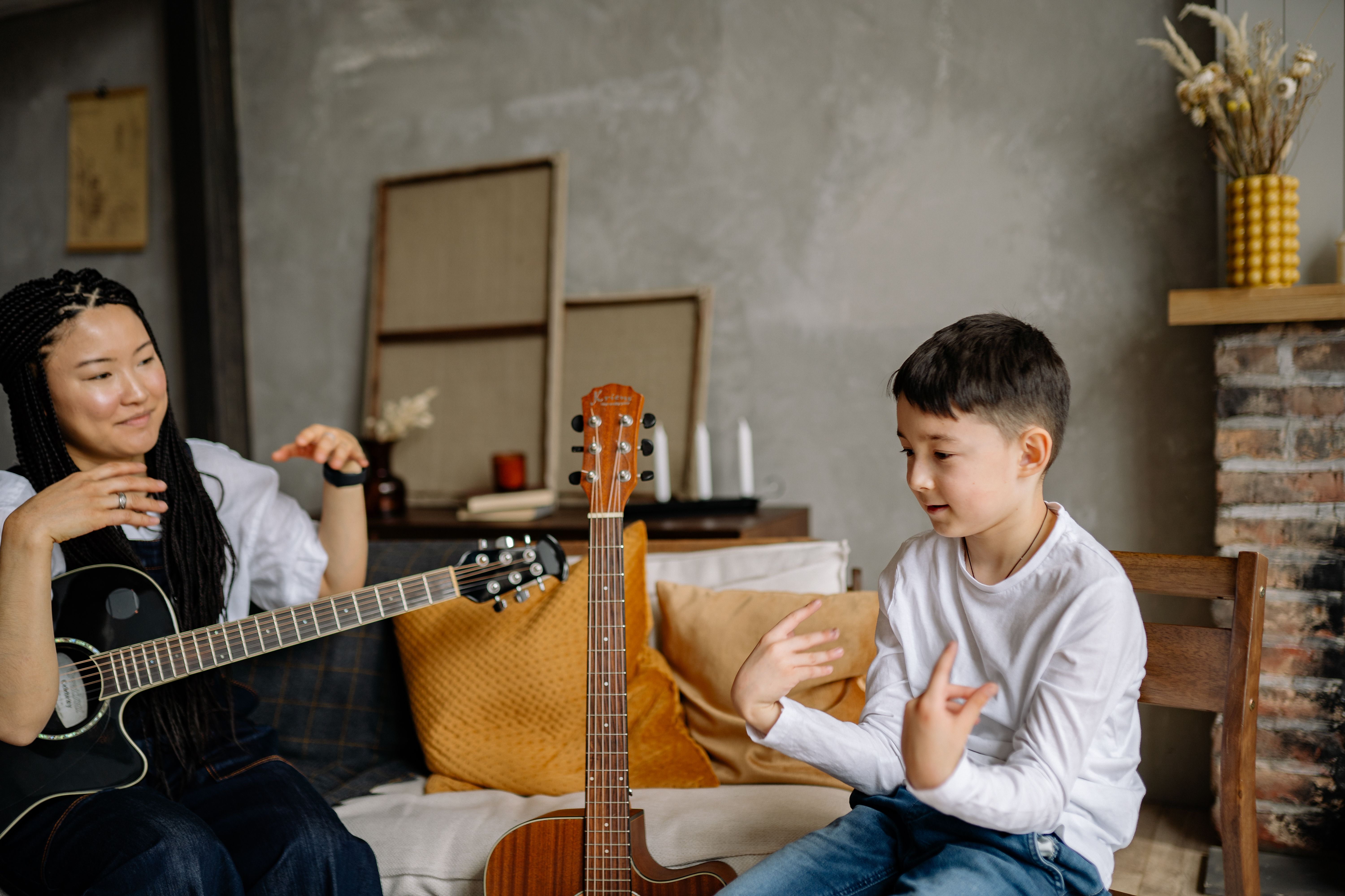 A woman teaching a boy how to play acoustic guitar in a cozy living room setting, fostering learning and communication.