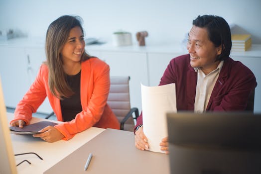 Two business professionals smiling and discussing documents in a modern office.