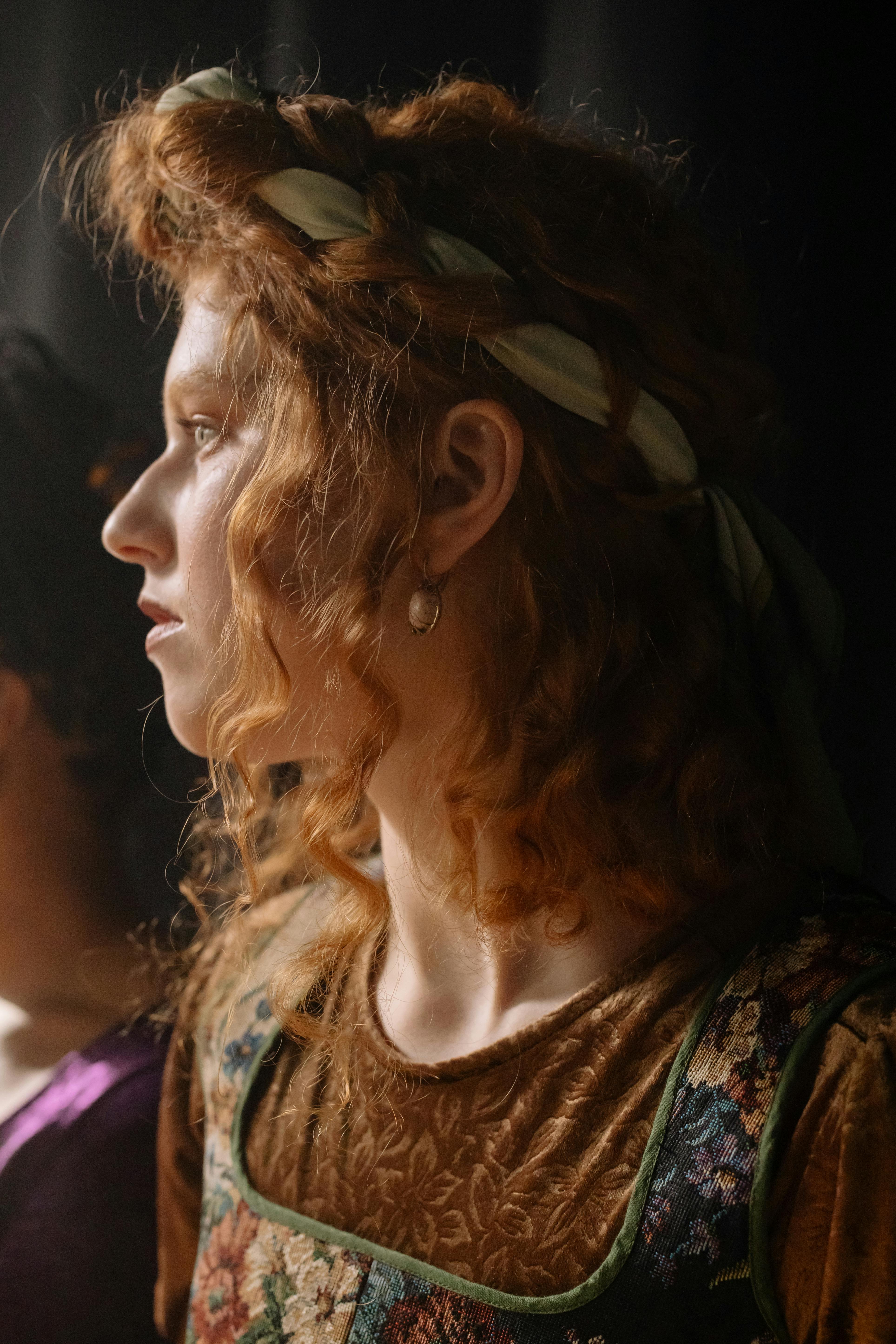 Profile of a redheaded woman in classic attire with soft, natural lighting and a floral headband.