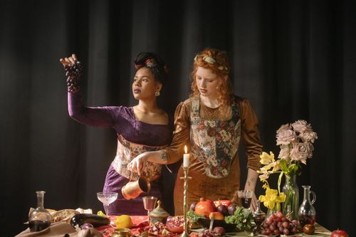 Free Two women in baroque-style dresses captured in a lavish indoor setting with fruits and candlelight. Stock Photo