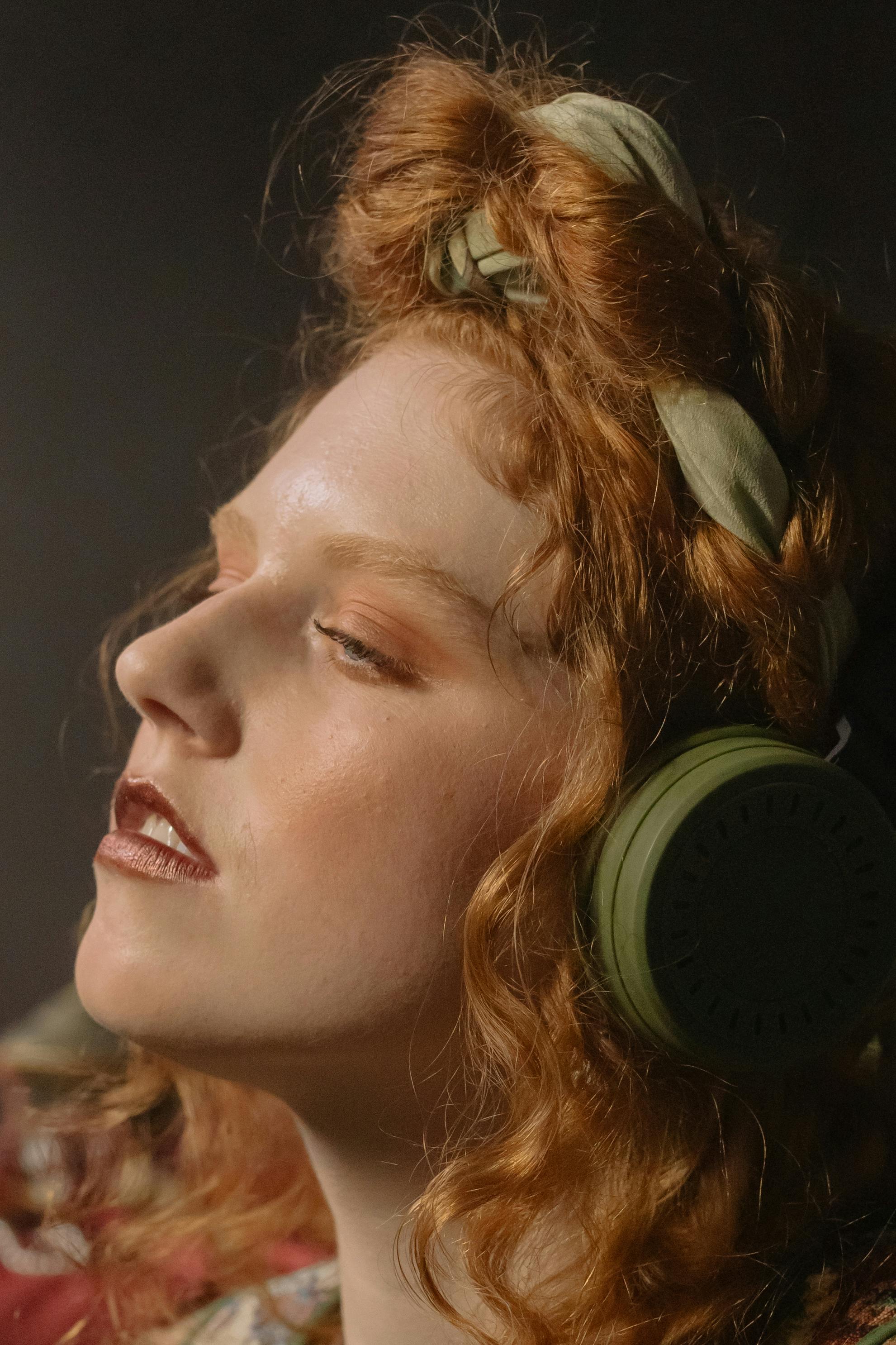 Close-up portrait of a redheaded woman wearing headphones and enjoying music with eyes closed.