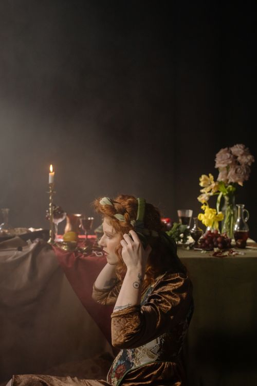 Free Redheaded woman in vintage attire enjoying music with headphones at a candlelit table. Stock Photo