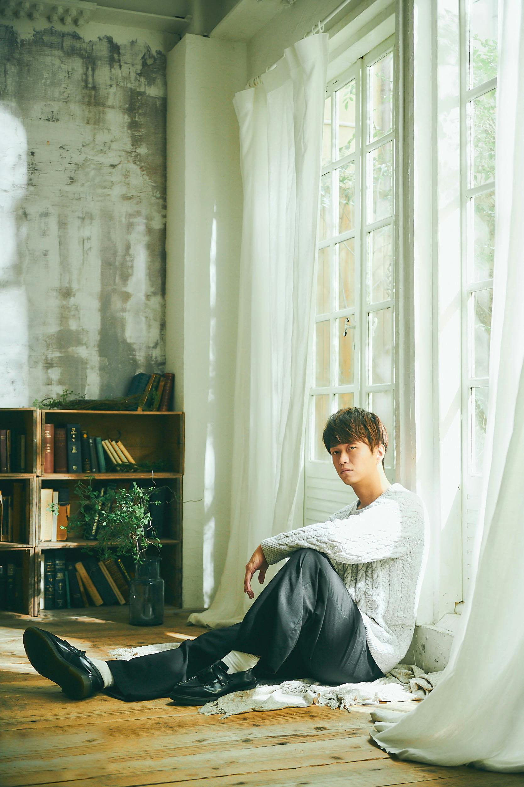Asian man sitting in a bright room by a window with a thoughtful expression, natural light.