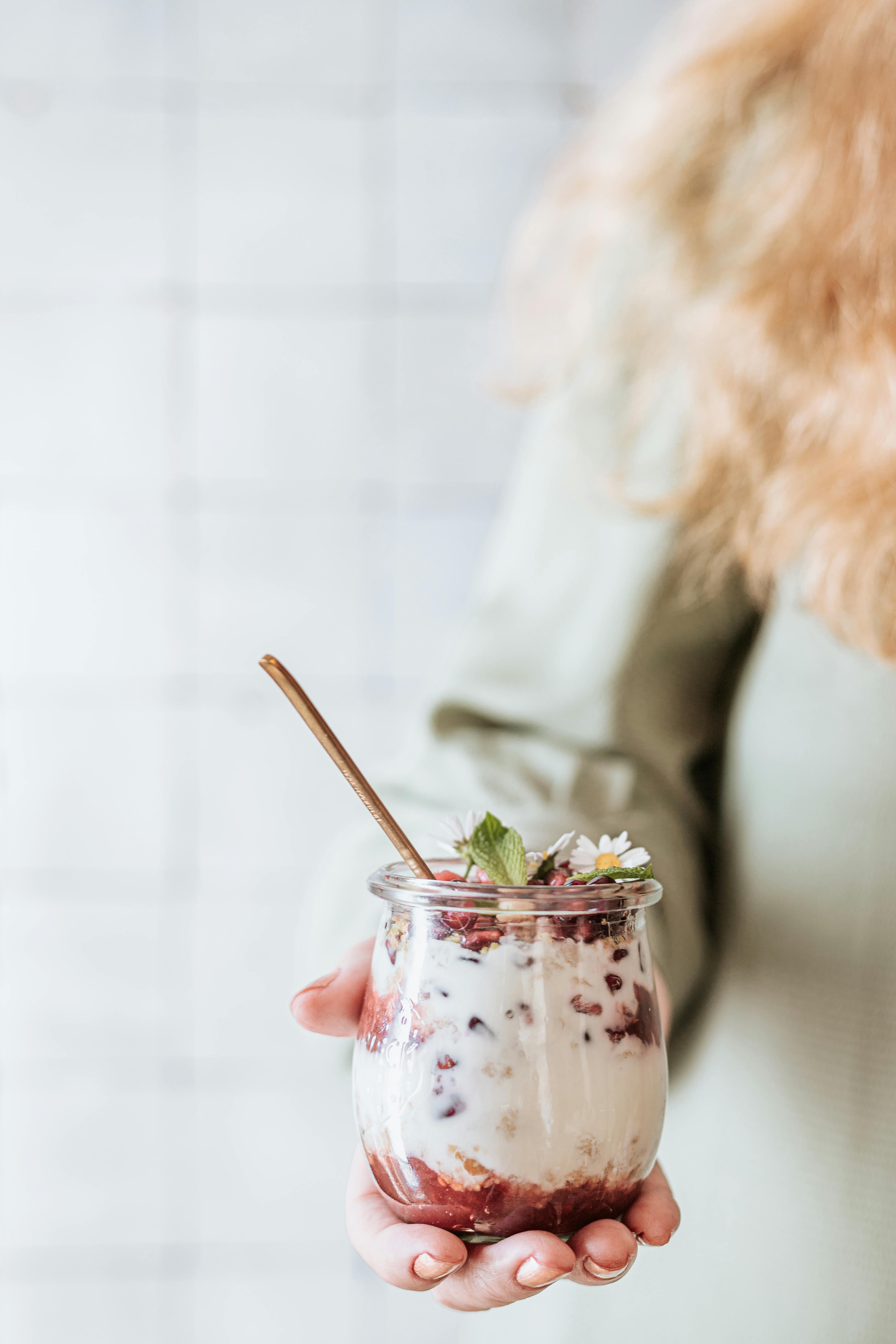 Close-up of a woman's hand holding a yogurt parfait with berries and granola.
