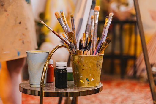Colorful collection of painting tools in an art studio, featuring paintbrushes in a bucket.