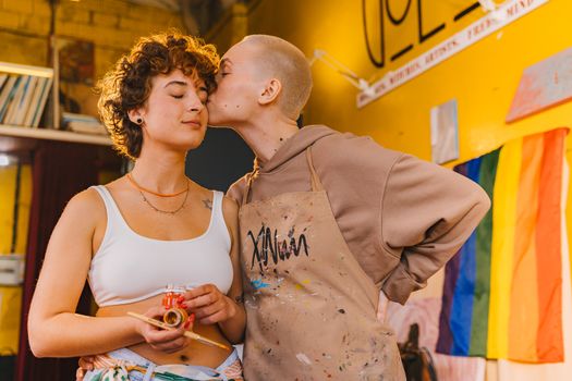 Two young women embrace creativity and love in an artistic studio setting.