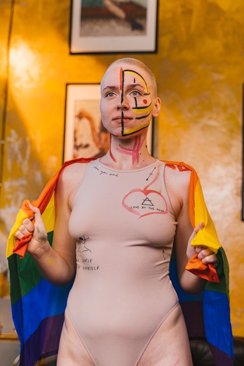 Free A vibrant portrait of a woman with face paint holding a rainbow flag indoors. Stock Photo