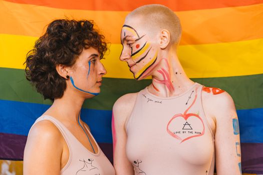 Artistic portrait of a couple with face paint against a rainbow flag backdrop, symbolizing diversity and love.