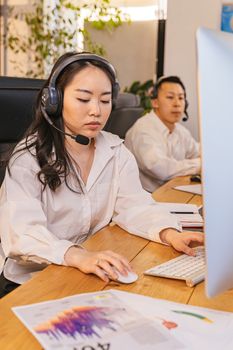Two professionals in headsets working on computers at a wooden desk, focused and engaged.