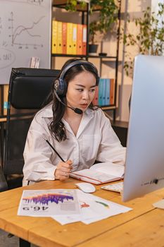 Businesswoman wearing headset, focused on computer work in modern office setting.