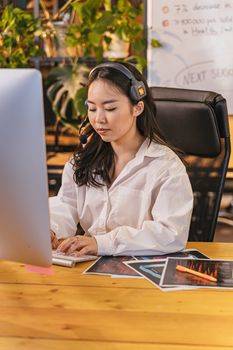 Young businesswoman in white shirt working at desk with headset and computer in modern office.