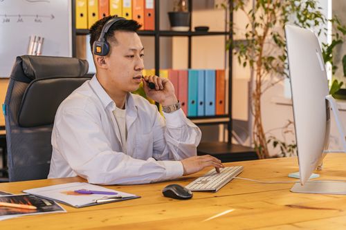 Free Businessman working at desk with computer and headset, in a modern office setting. Stock Photo