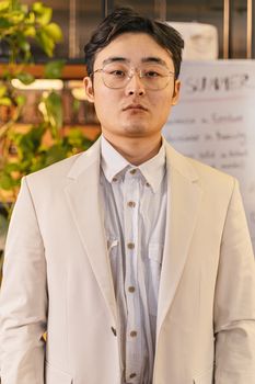 Confident young man in glasses posing indoors in a white suit. Stylish and modern.