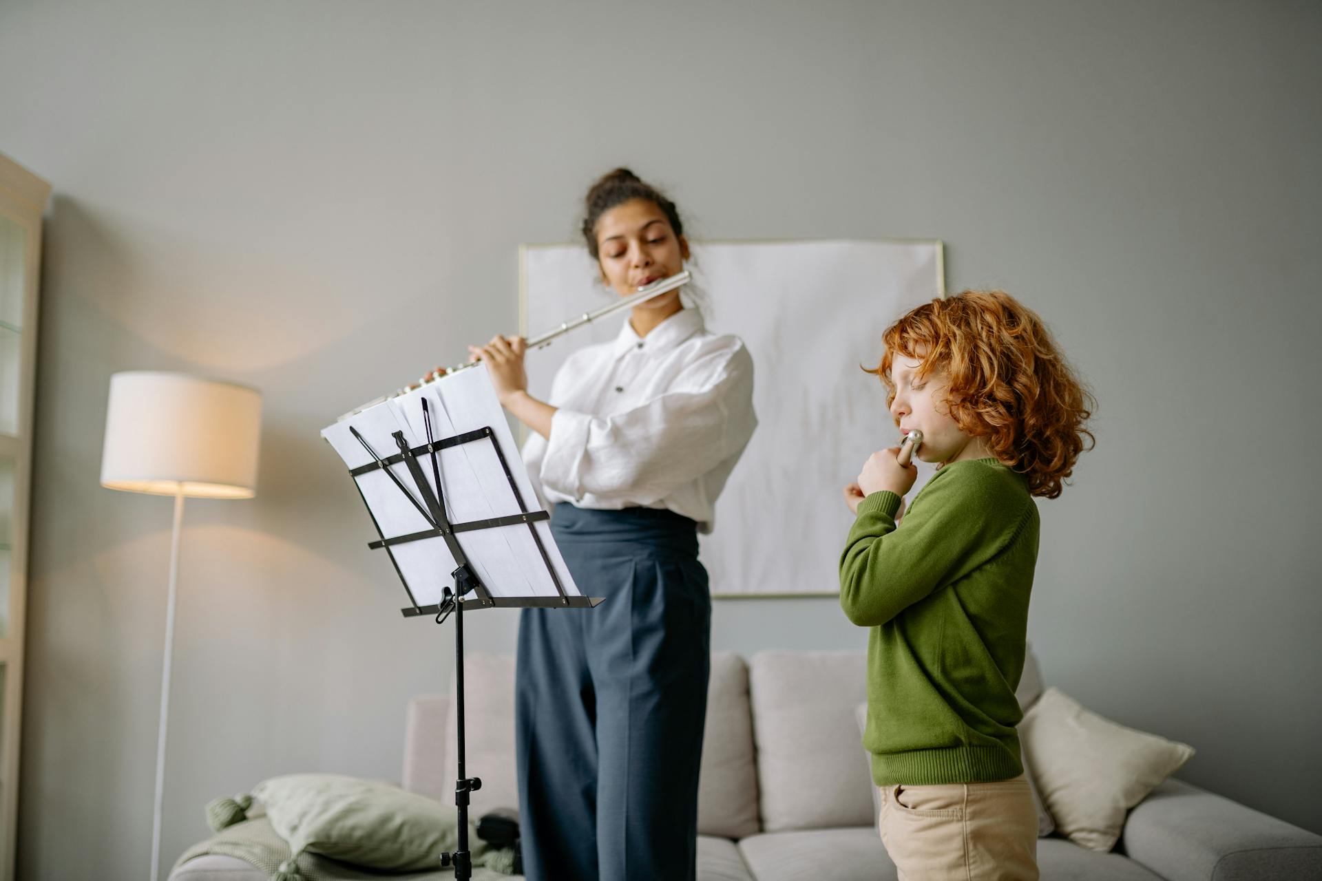 A woman teaching a young boy to play the flute indoors during a music lesson.