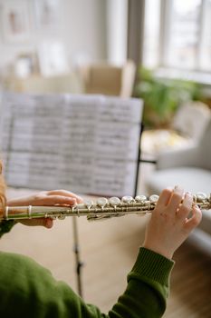 A child practices playing the flute at home with a music sheet in the background.