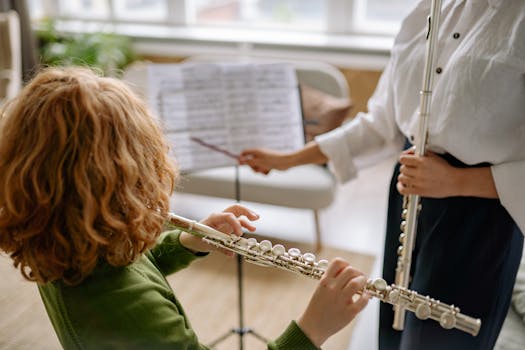 A child receiving a flute lesson from a teacher indoors, focused on music sheets.