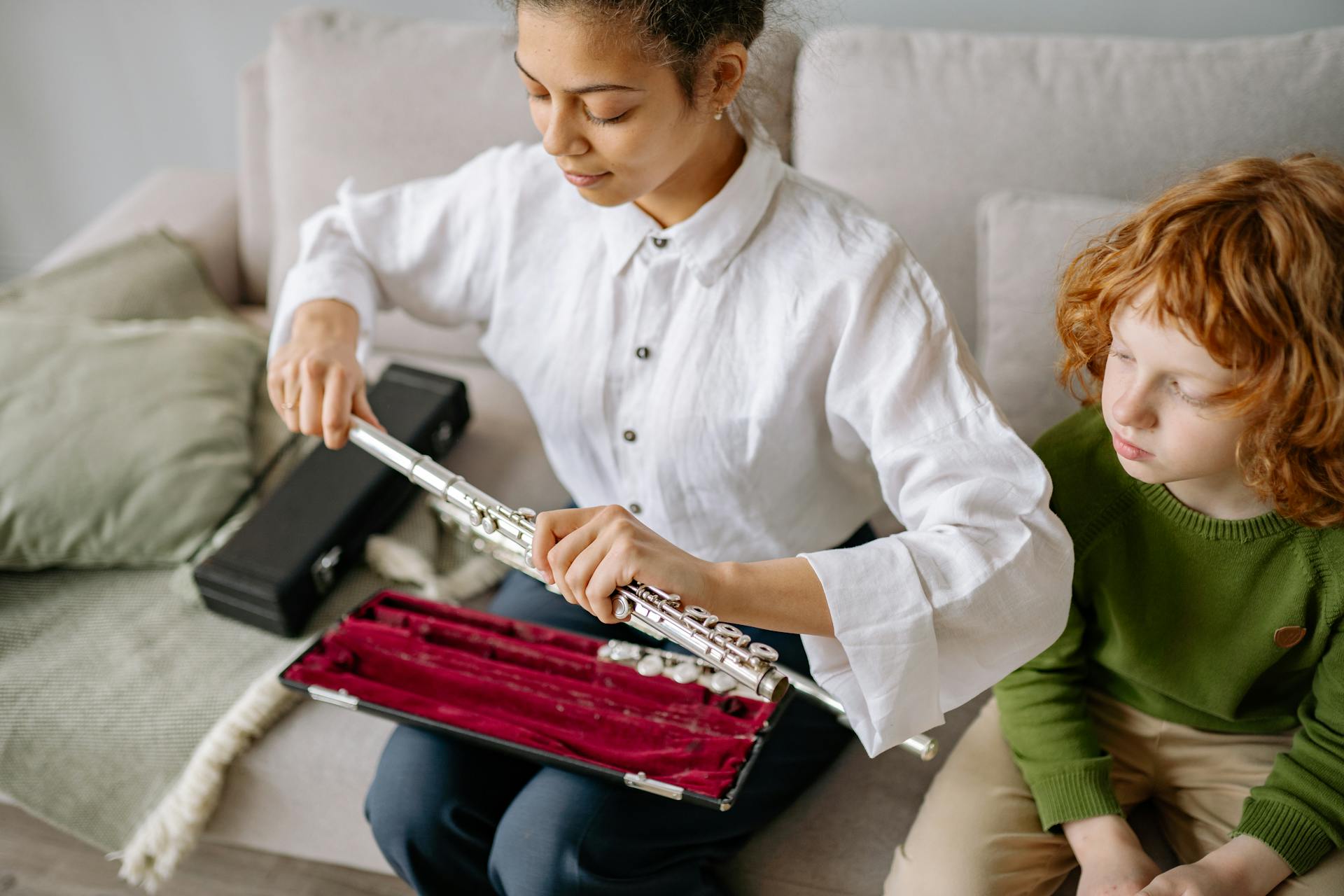A teacher helps a student assemble a flute on a sofa, enhancing musical skills.