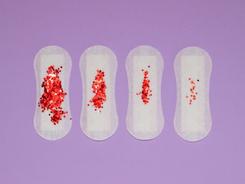 Free Four menstrual pads with red glitter, symbolizing menstruation, on a purple surface. Stock Photo