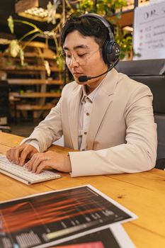 Adult man wearing a headset and eyeglasses, working at a desk in a modern indoor office space.