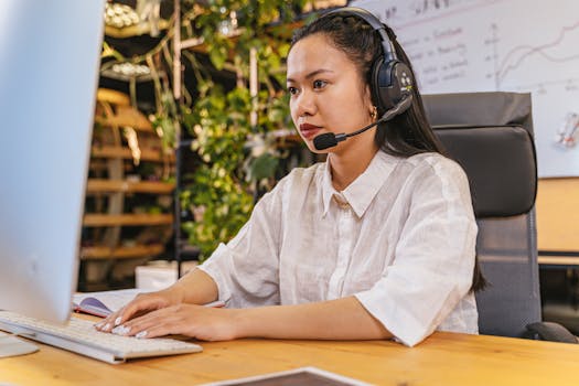 Professional woman using a computer and headset in a modern home office setting.