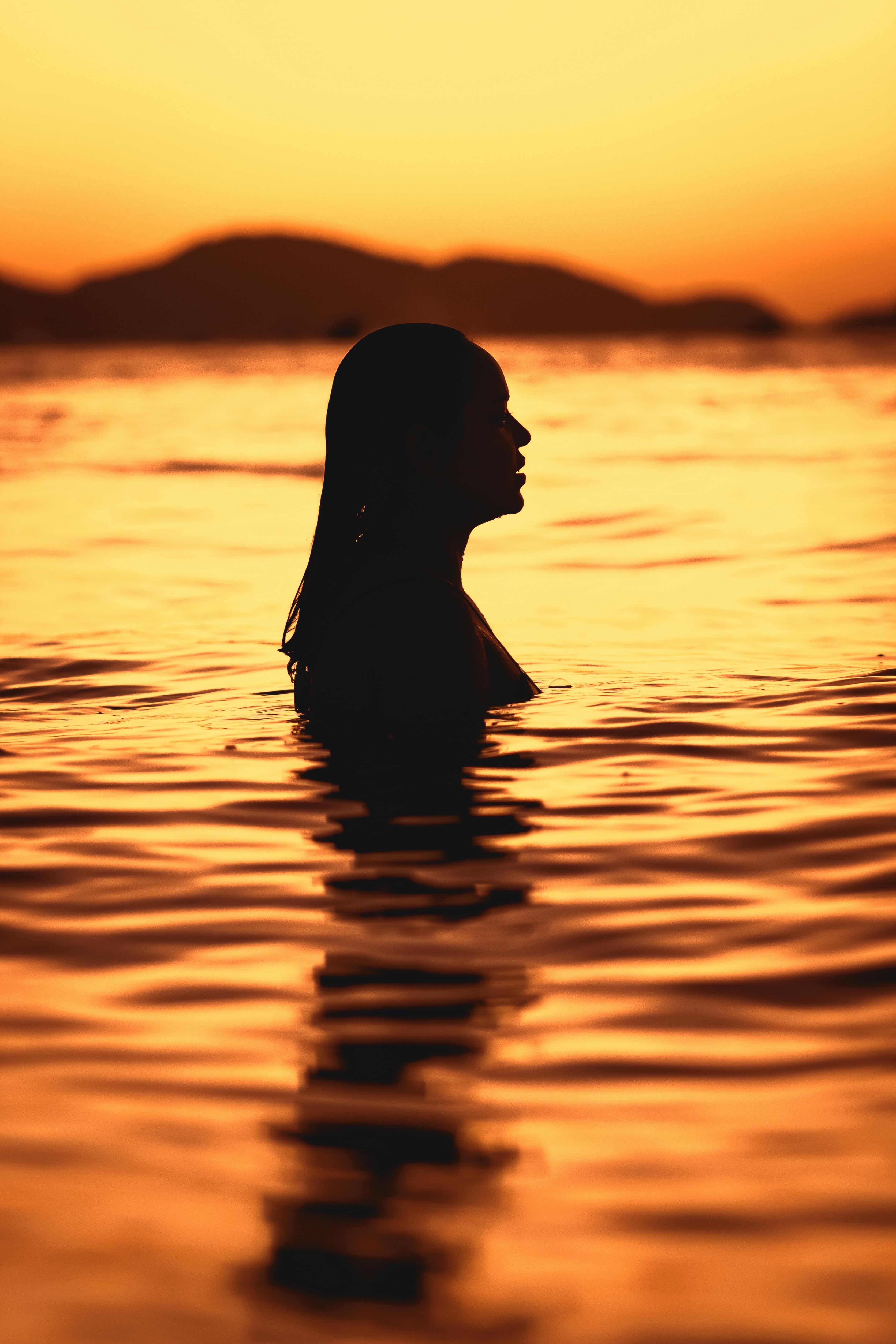 Silhouette of a woman standing in water during a beautiful sunset.