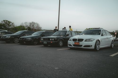 Free A lineup of BMW cars parked in an outdoor lot with people gathering during the evening. Stock Photo