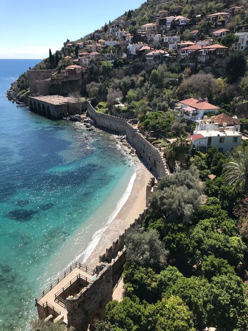 Free Aerial view of a coastal village with lush greenery, historical walls, and a serene beach. Stock Photo