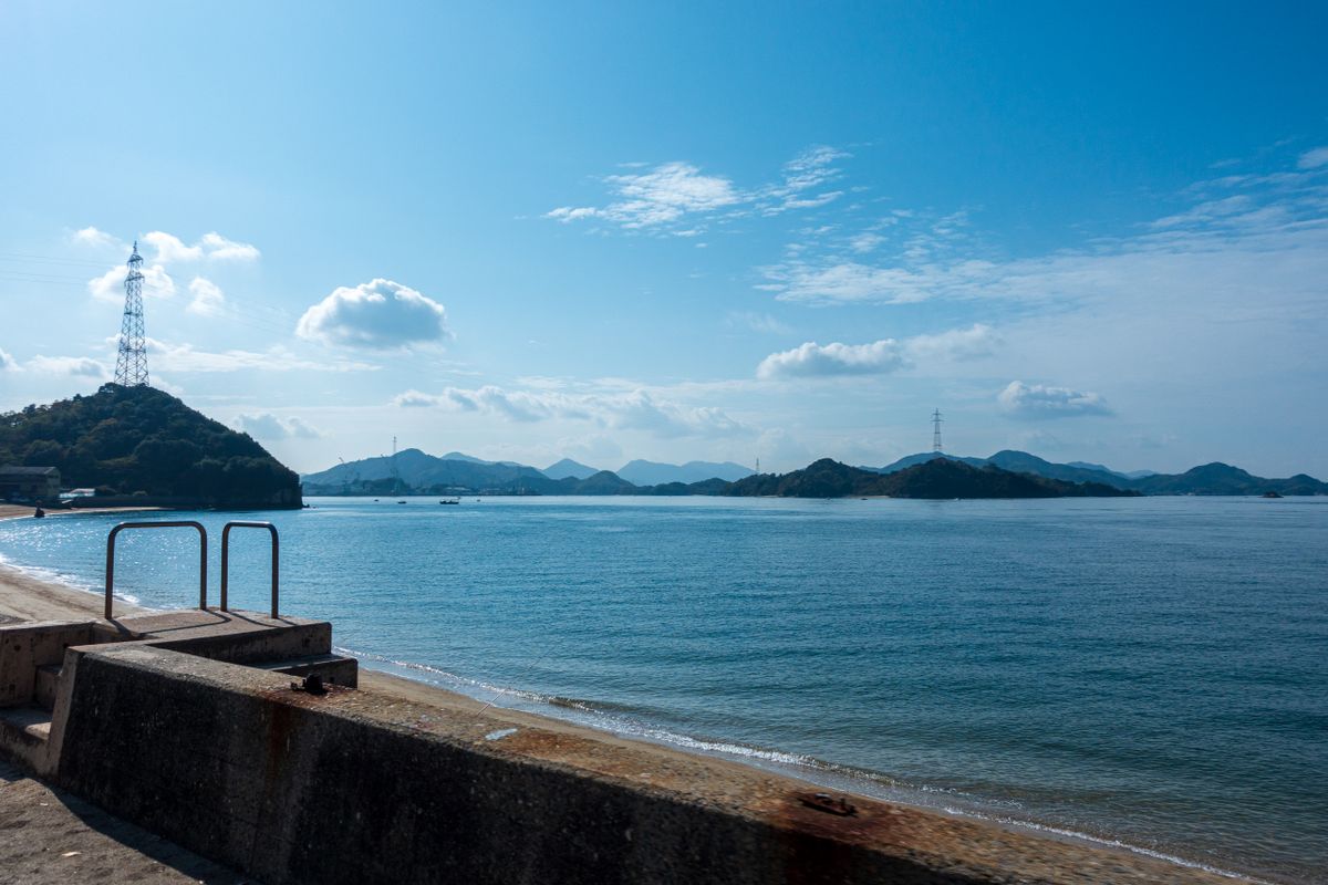 Stone seaside embankment with blue sky and islands at Onomichi in Hiroshima, illustrating the historic stone harbor works found near Tomonoura