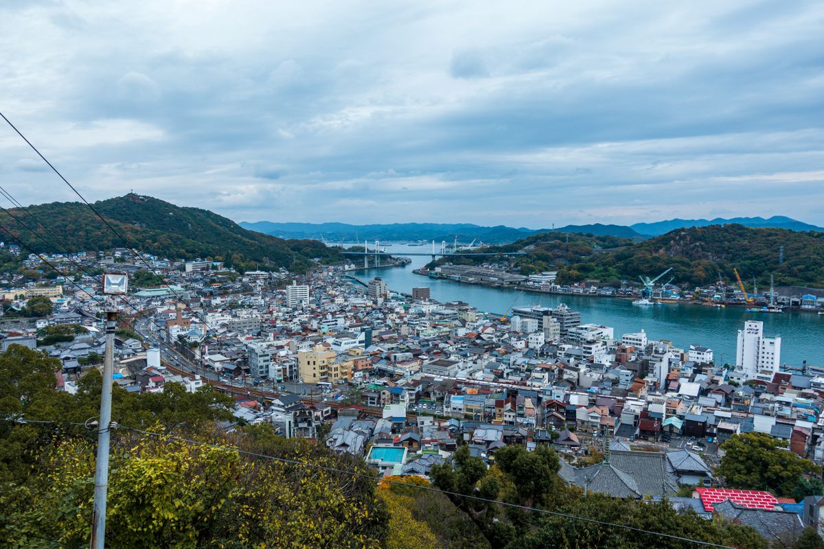 Aerial view of a Japanese coastal town with a river and green hills meeting the Seto Inland Sea, similar to the hillside setting of Tomonoura