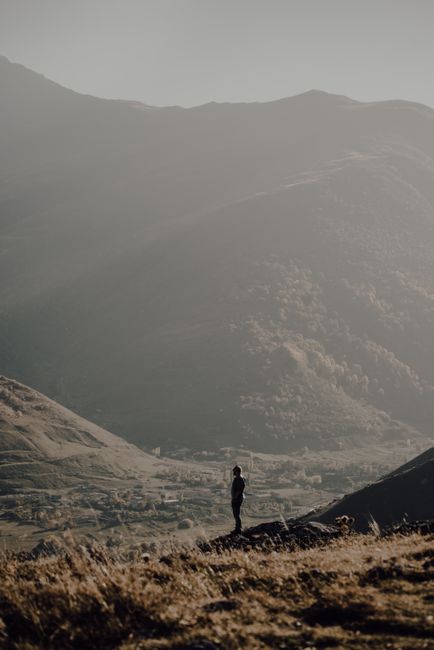 A lone man stands amidst vast mountains, under a soft, muted sky.